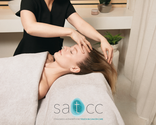 Lady laying down on a light gray spa massage table receivng a facial massage with the SATCC logo displayed over the top