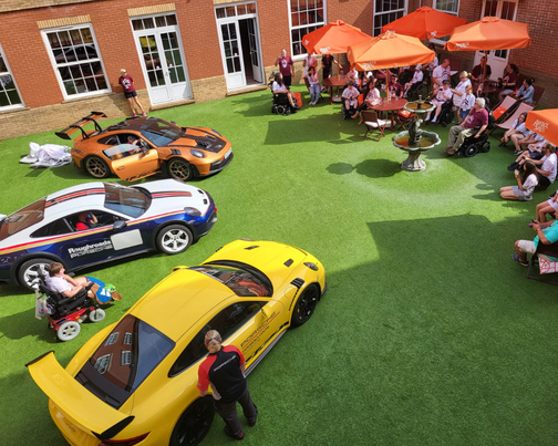 Three sports cars on a green astro turf with people viewing them