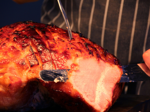 A close-up of a chef carving a joint of marmalade gammon