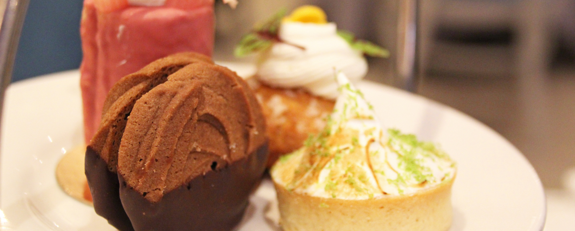 A close-up of a sweet spring afternoon tea plate with a chocolate victoria biscuit, lime meringue tart, and strawberry layered cake in the background