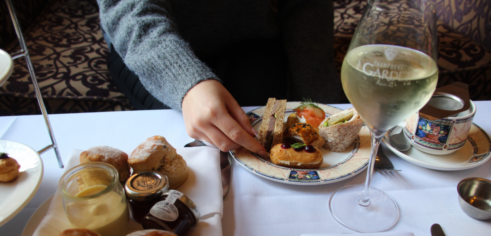 A lady in a grey sweater plating up her afternoon tea next to a glass of prosecco