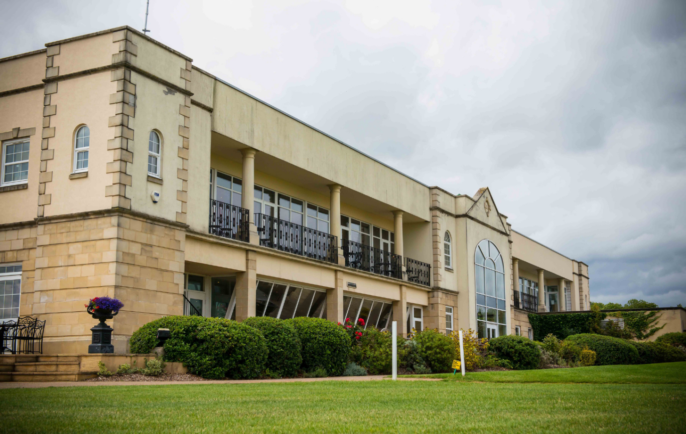 An exterior shot of a white golf clubhouse overlooking a putting green