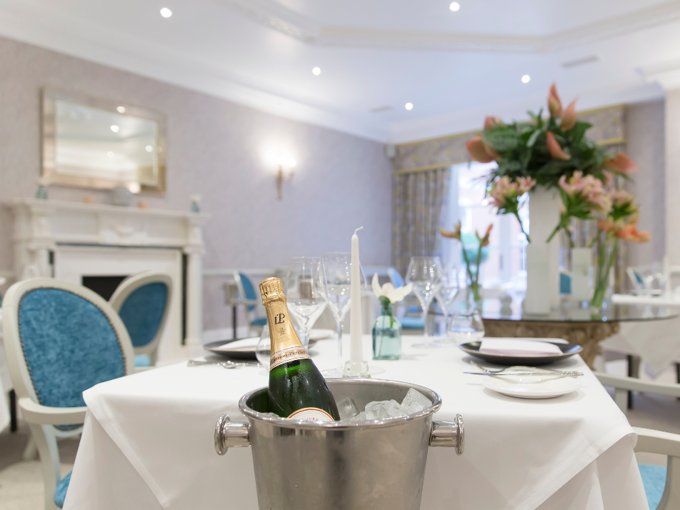 Inside a fine dining restaurant with white tables, blue chairs, champagne and glasses, and a flower centre piece in the room