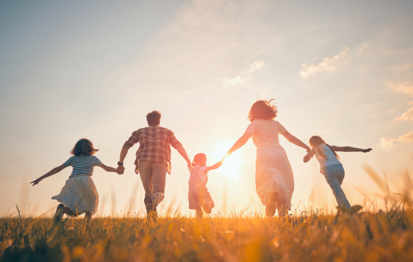 A family of 5 running through a field towards a sunset