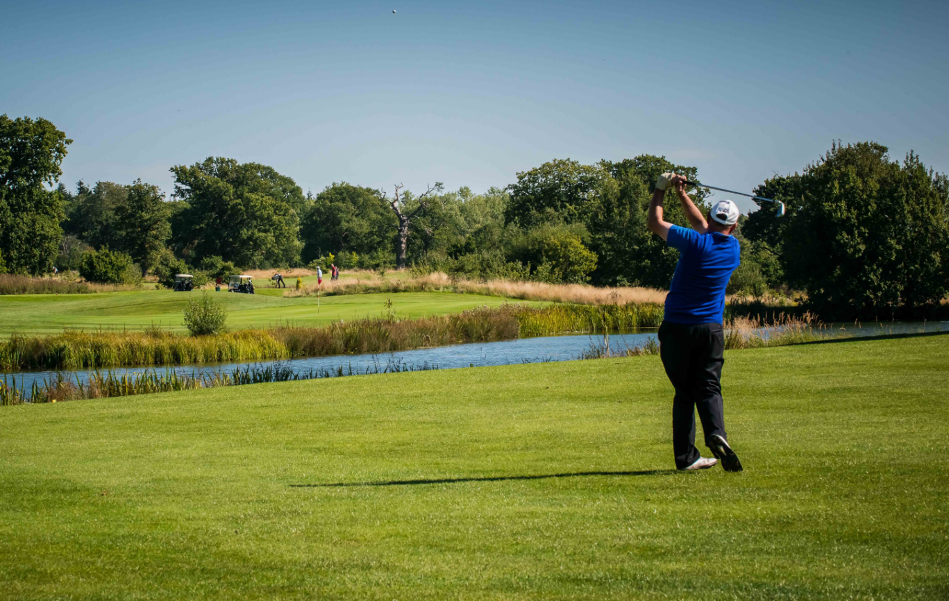 A golfer taking a swing down the green overlooking a lake on a sunny day