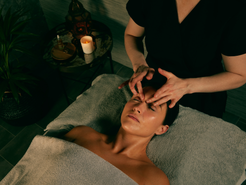 A lady laying on a grey massage bed receiving a facial treatment