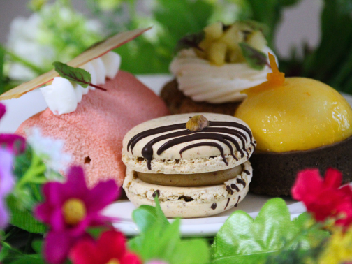 A plate of sweet goods, made up of a chocolate macaron, raspberry rhubarb roulade, and lemon & chocolate chart, decorated in spring flowers