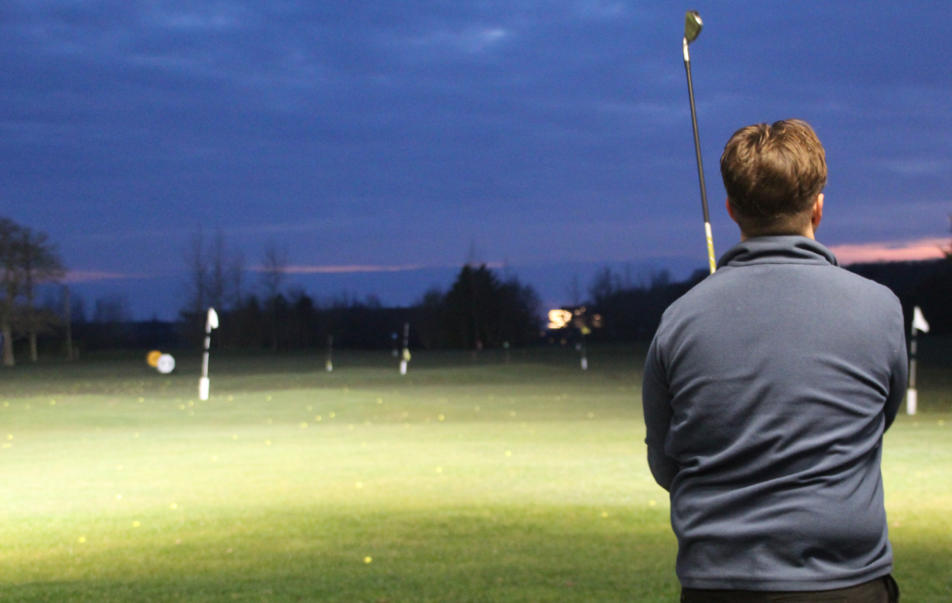 A man viewing down a golf driving range with his golf club