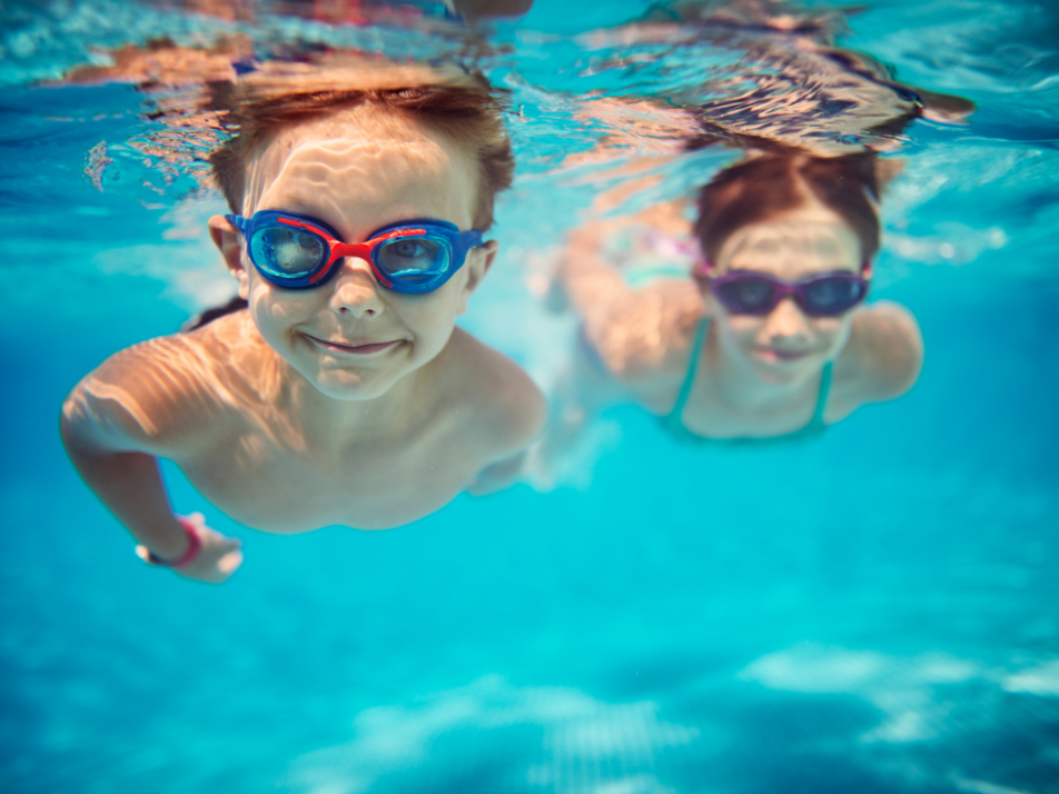 Two children swimming under water in a swimming pool with goggles on