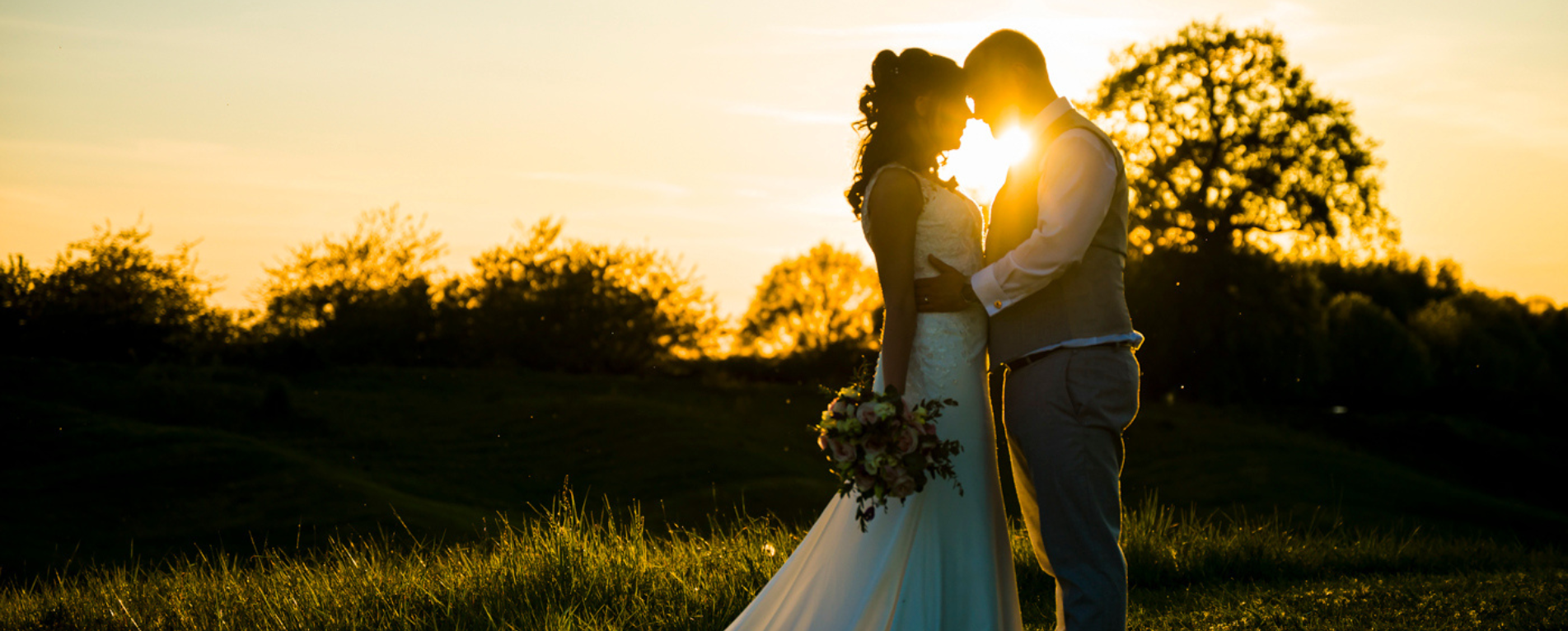 A couple standing infront of a sunset embracing each other on their wedding day