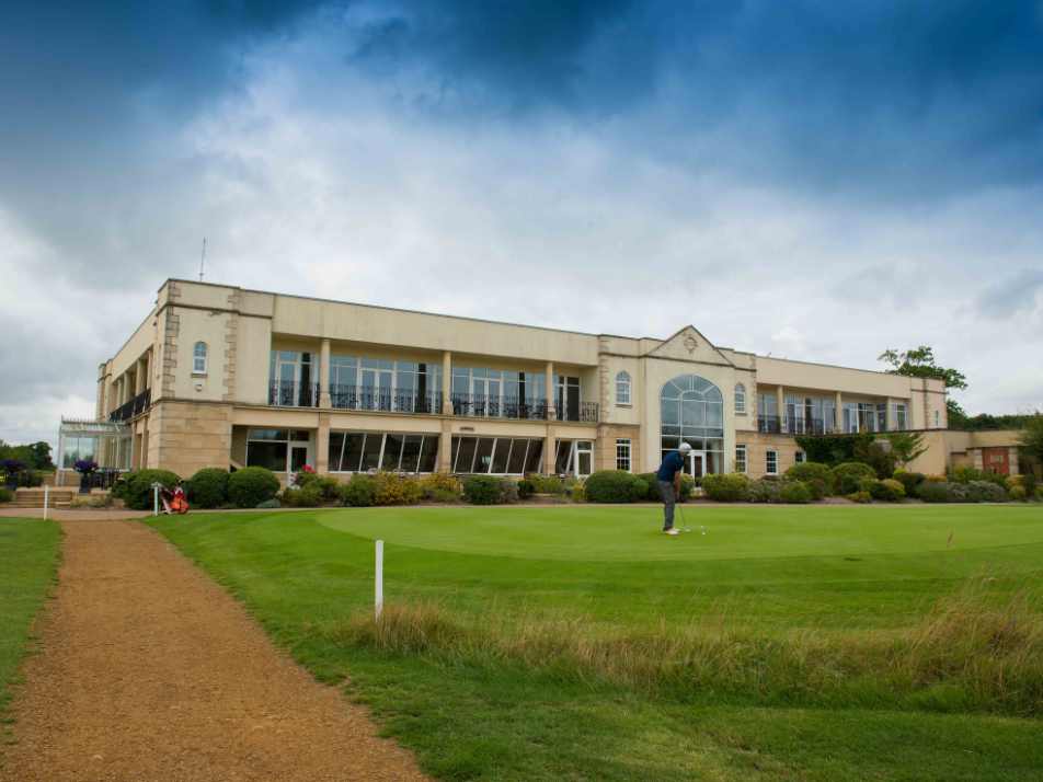 Outside view of a golf clubhouse with window panels on a white brick building facing towards a putting green