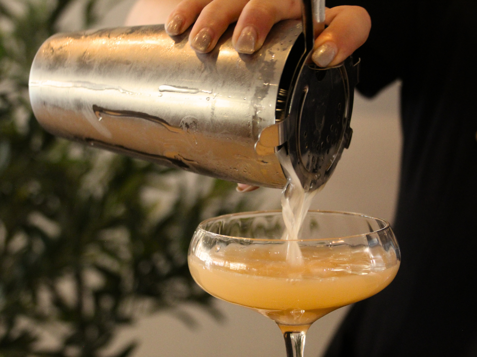 A bartender pouring a cocktail shaker into a martini glass