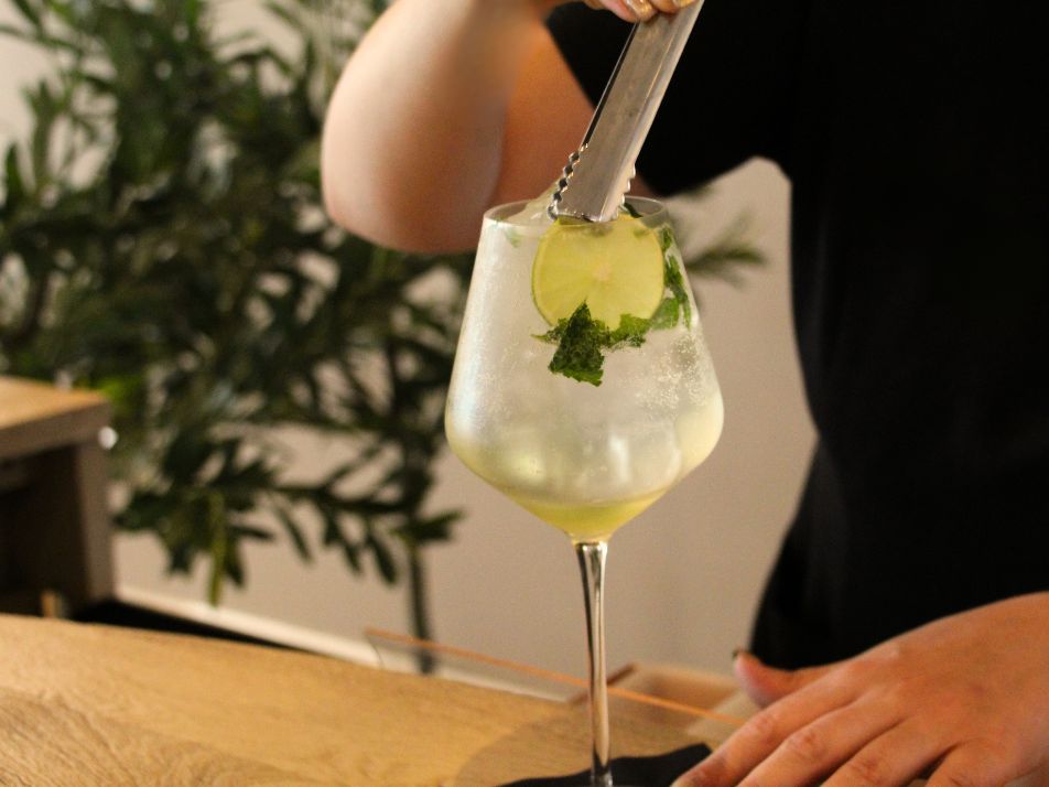 A bartender stirring a gin and tonic cocktail garnished with lime and mint
