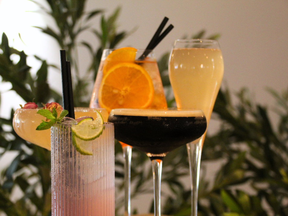 An espresso martini, aperol spritz, bellini and cherry tumbler cocktail sitting infront of a green bush