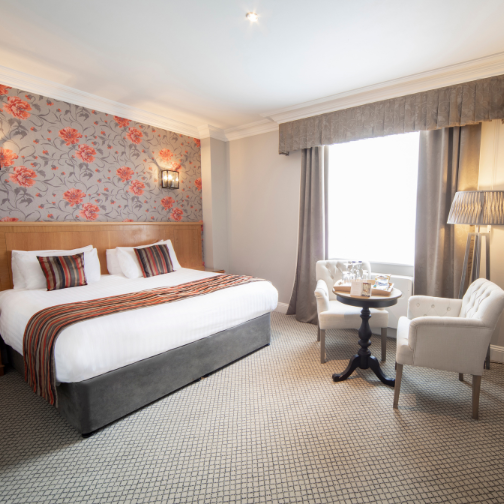 A hotel bedroom with grey chairs and a table with inclusive sweets