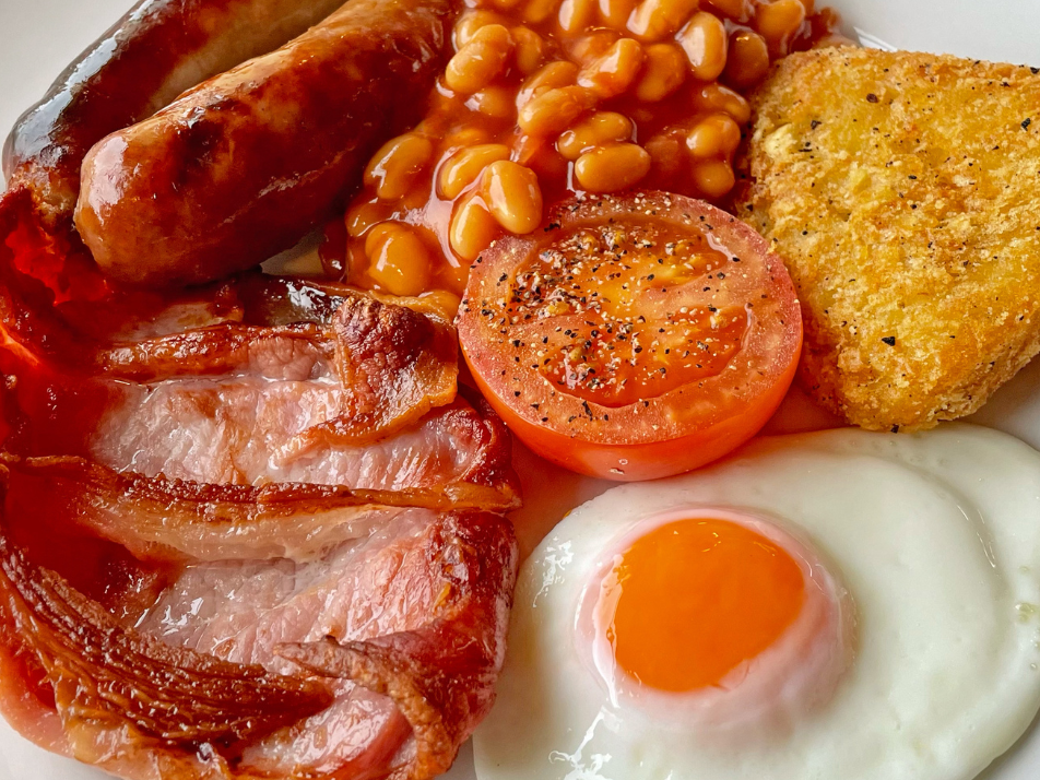 A close up of a full english breakfast made up of a fried egg, bacon, beans and sausage