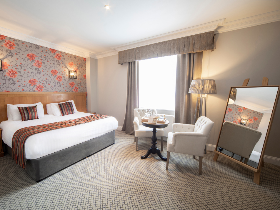 A hotel bedroom with grey chairs and a table with inclusive sweets