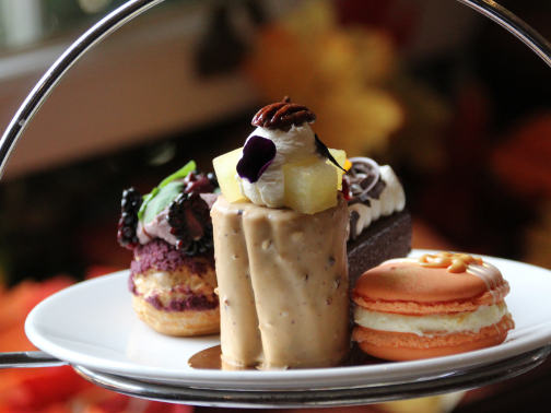 A plate of afternoon tea sweet pastries in autumn colours and autumn leaves behind it