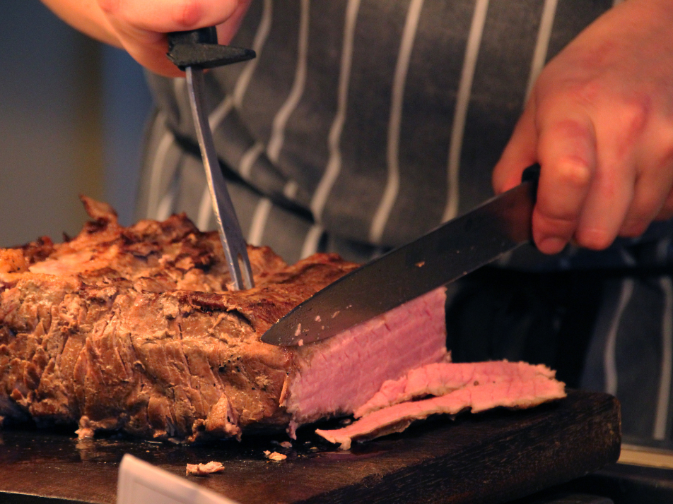 A carvery chef cutting slices into a medium rare sirloin of beef